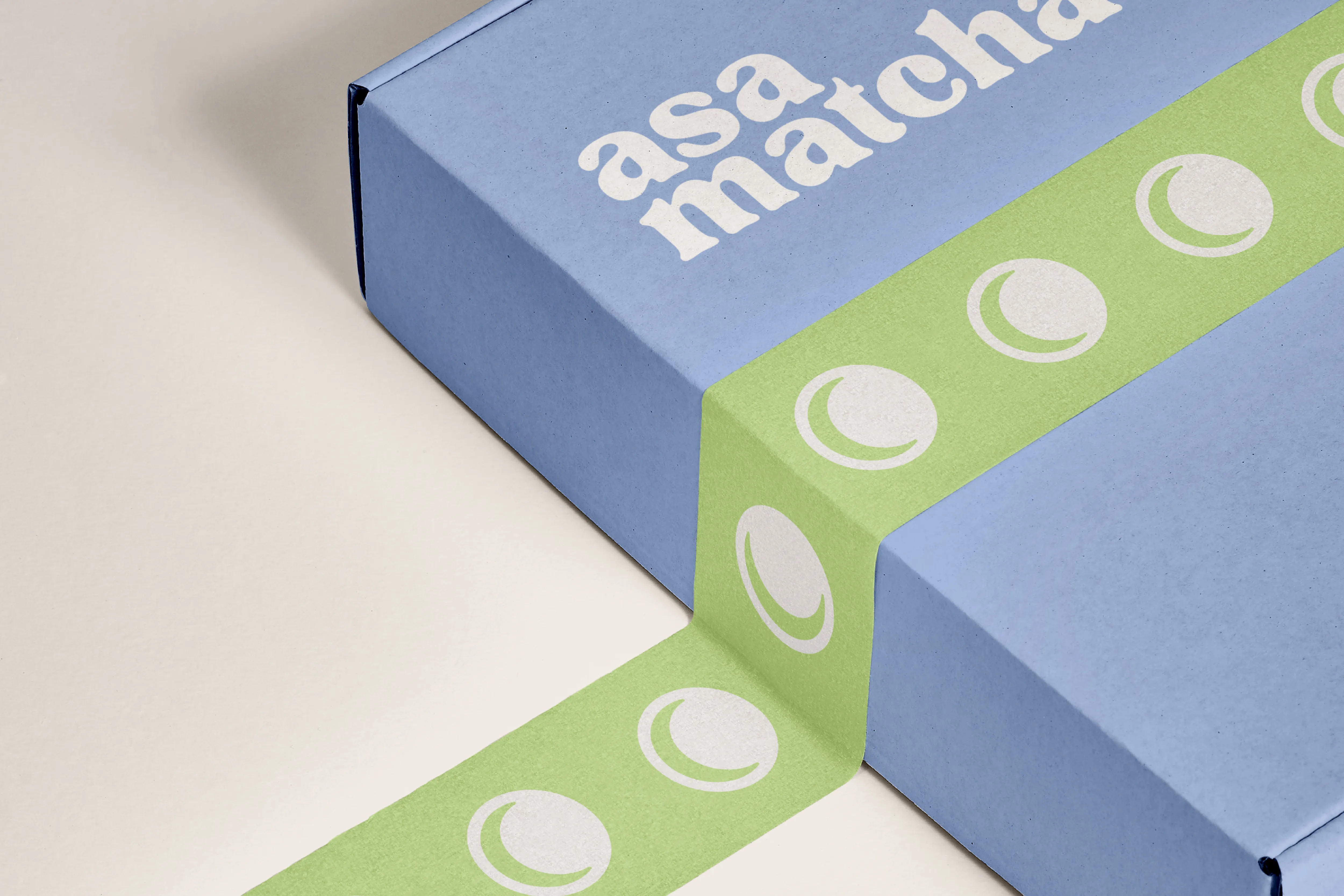 Blue Asa Matcha shipping box wrapped in green tape printed with the sun-and-moon logo