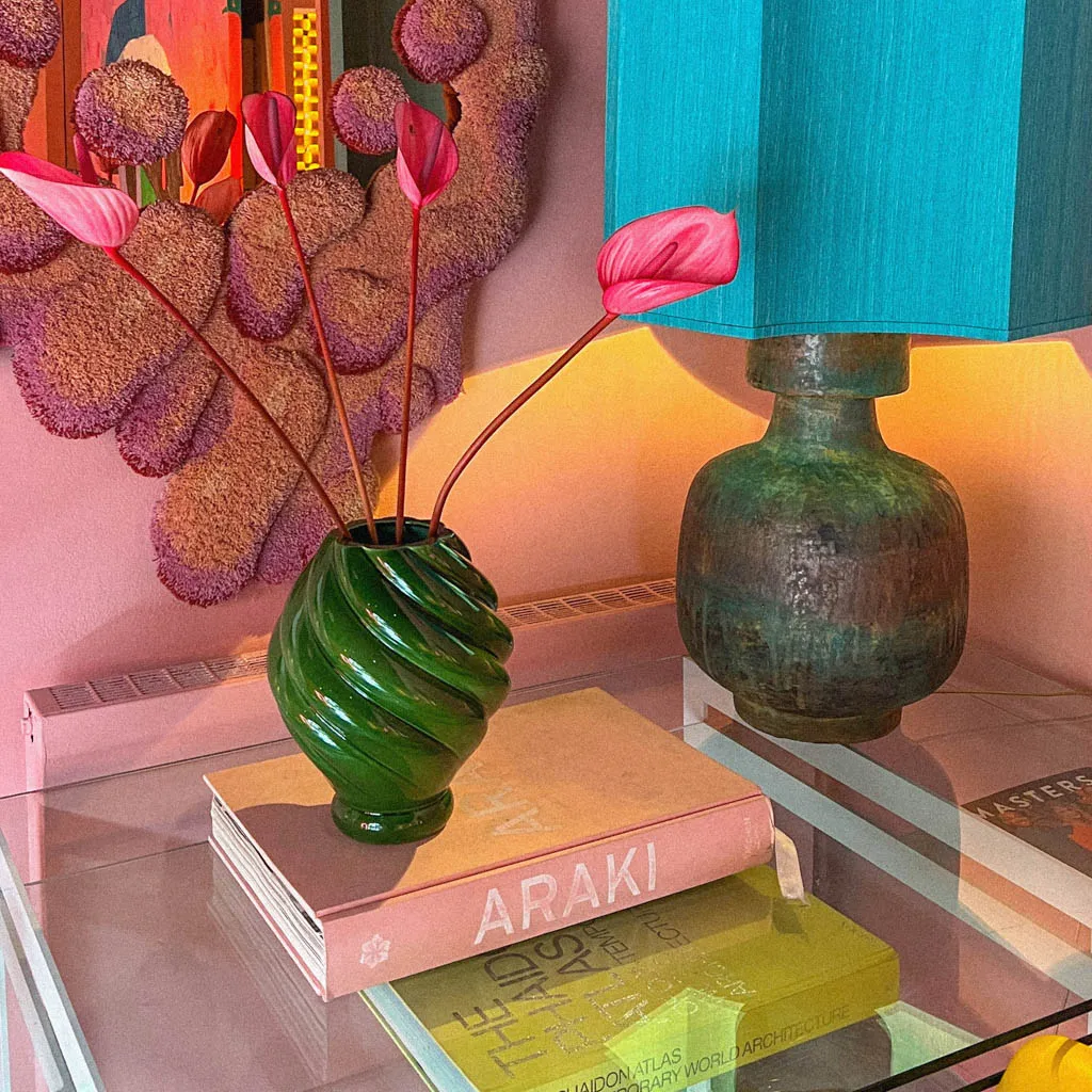 Green twisted ceramic vase with pink anthurium on a coffee table book beside a bronze lamp