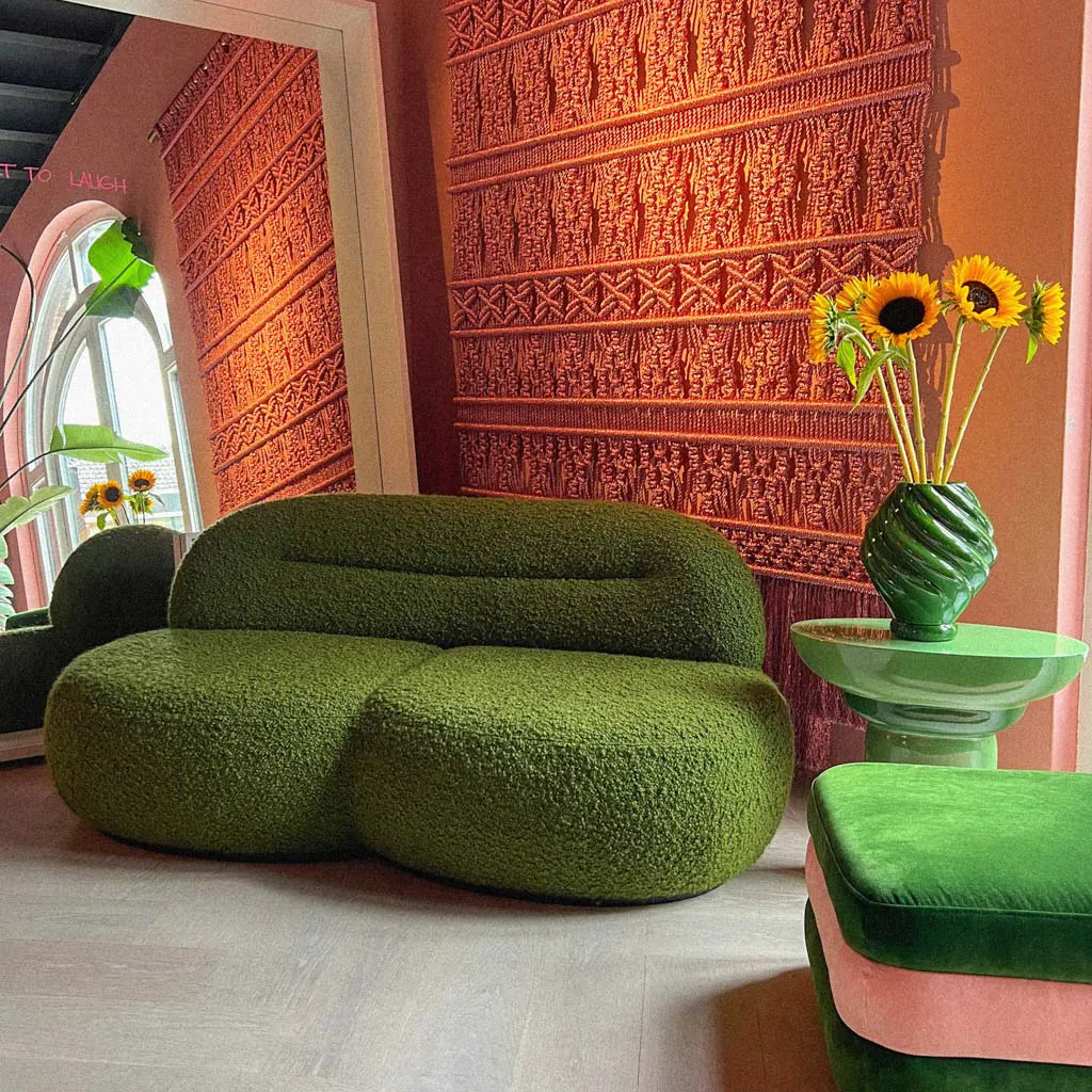 Moss-green bouclé sofa and a green side table with sunflowers against a terracotta macramé wall