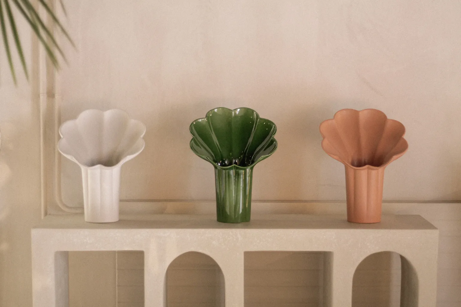 Three scalloped flower vases in white, green and terracotta on an arched white console