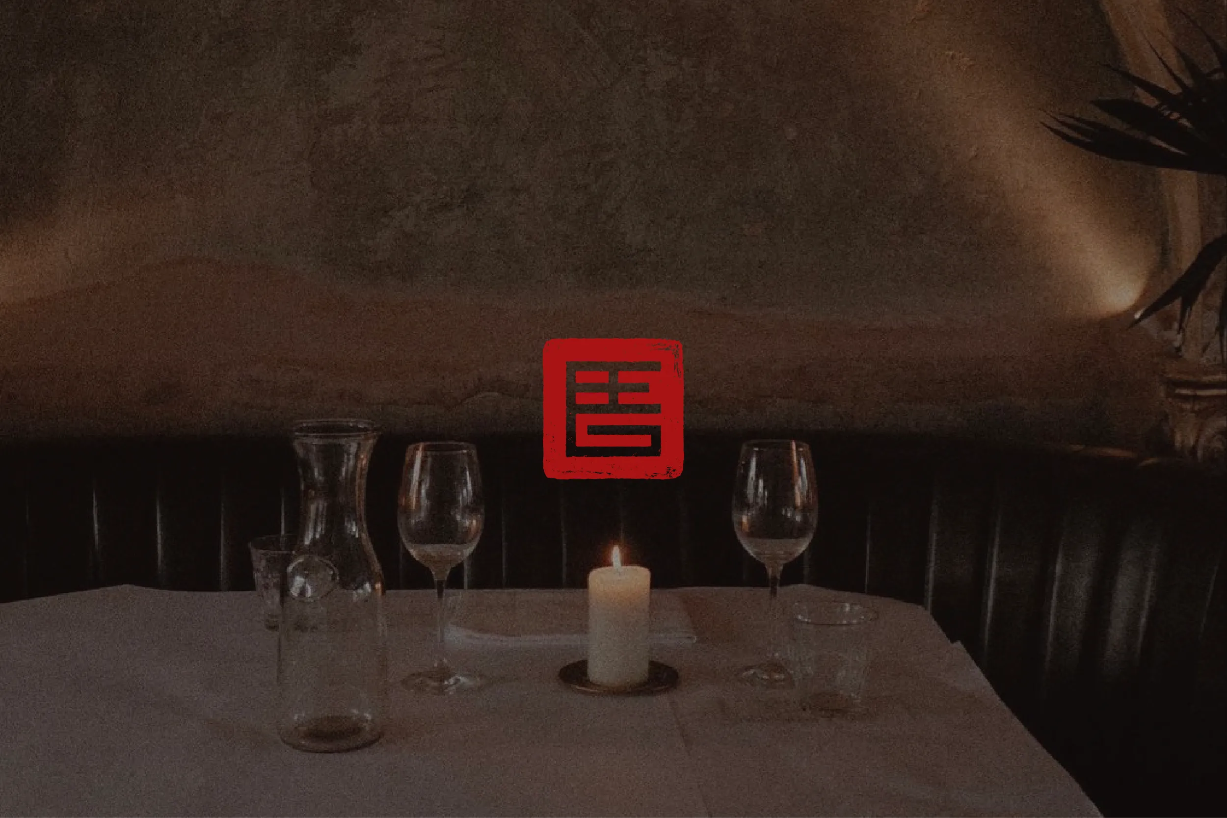 Red hanko-style seal over a candlelit restaurant table set with wine glasses