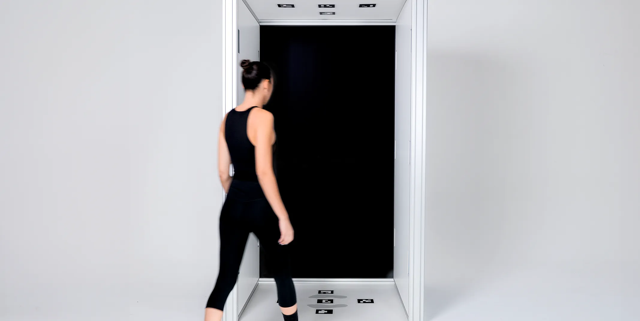 Woman in black activewear stepping into a white body-scanning booth