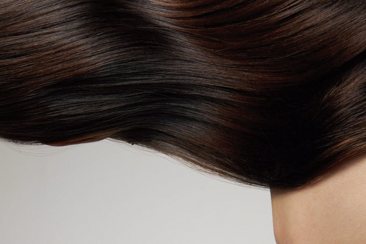 Animated sequence of glossy dark hair, wet curls on skin and a hair oil bottle beside white flowers