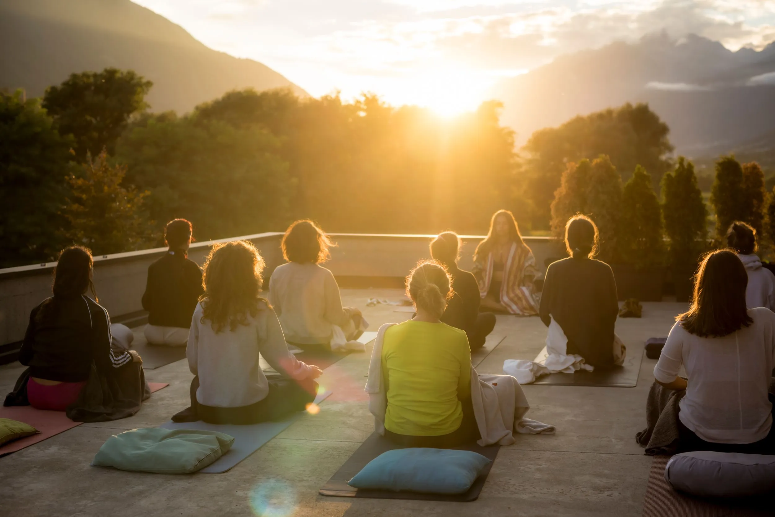 Group meditating on a rooftop terrace at sunset, with mountains behind